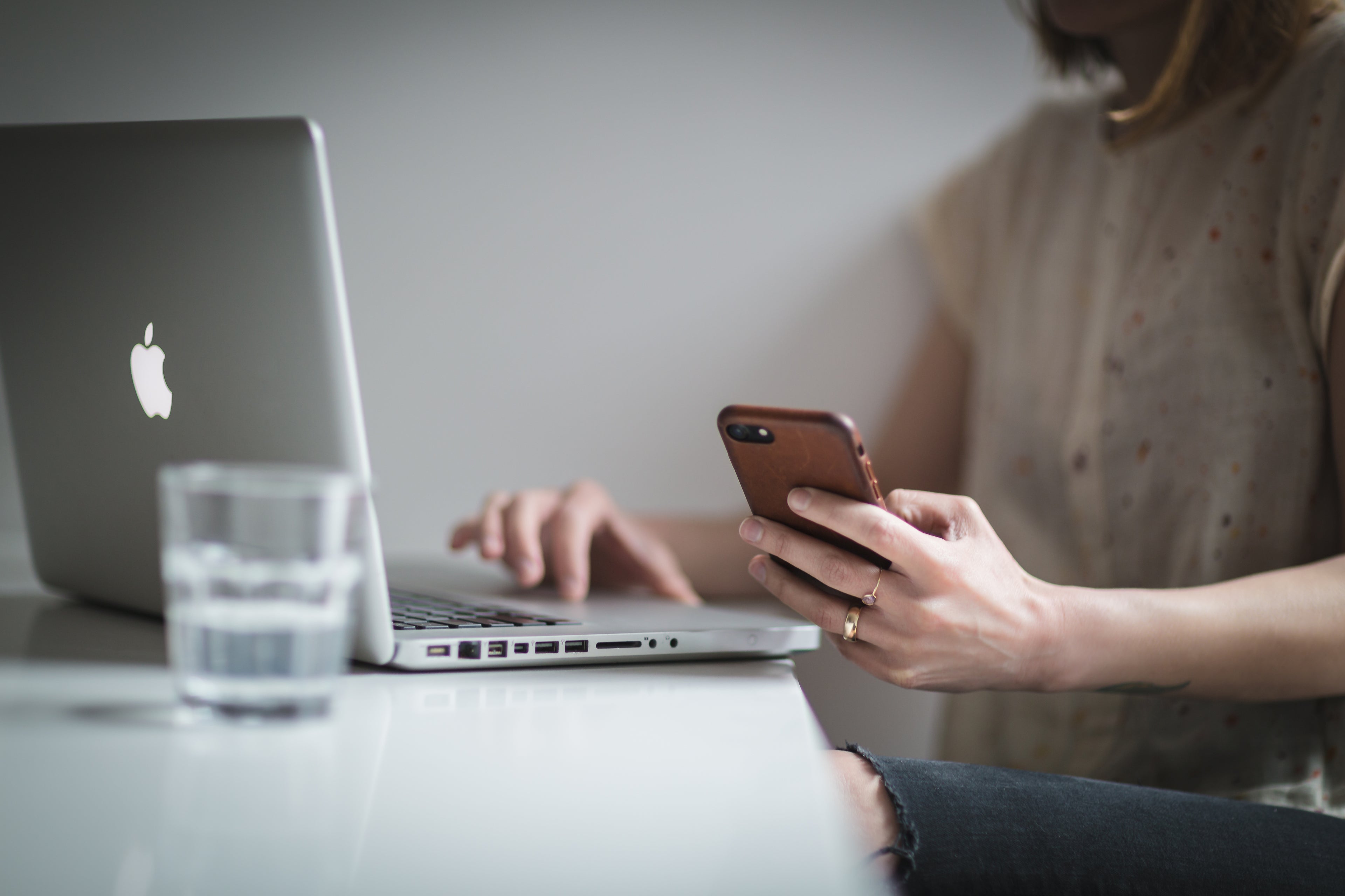 Kvinne sitter foran Mac-en og holder en iPhone 